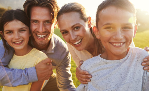 Portrait of happy white family embracing outdoors, backlit